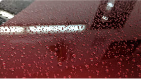 Water droplets on a section of a car to show the water beading capability of auto detailing
