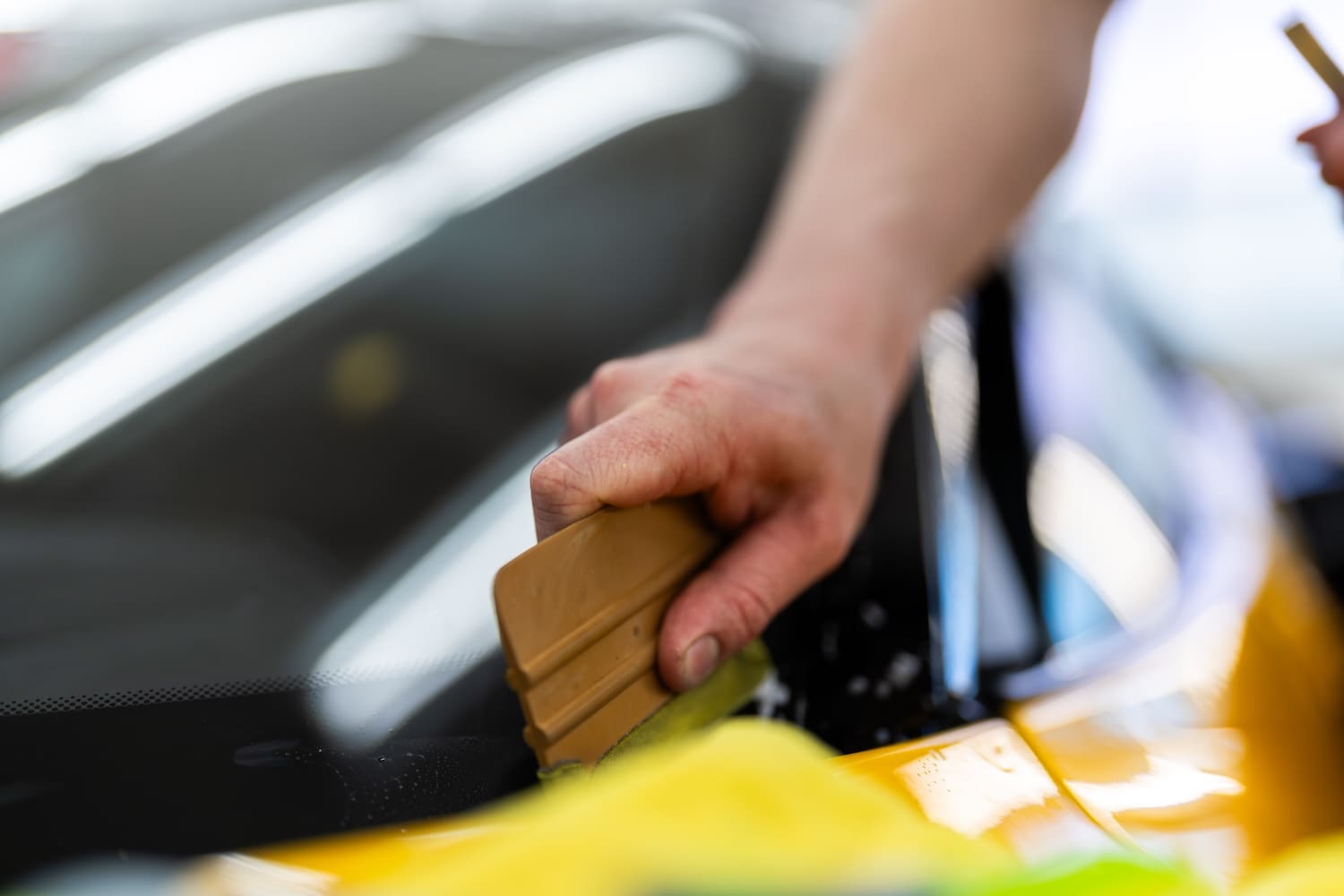 Squeegee in hand, working out bubbles on freshly applied tint on yellow car