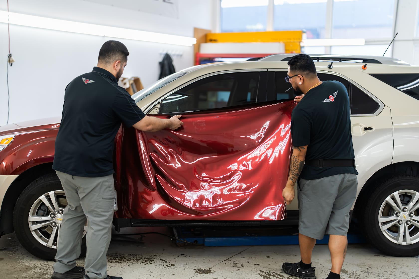2 guys applying a red PPF color change film over a tan SUV