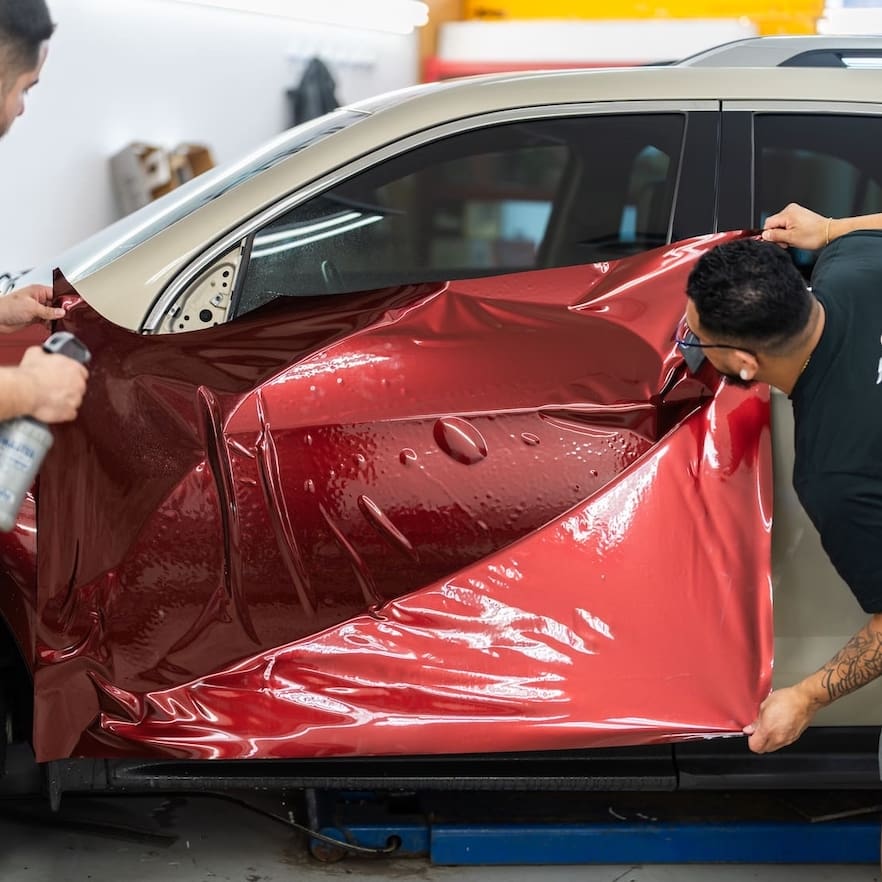 Two men laying red PFF on a gold SUV