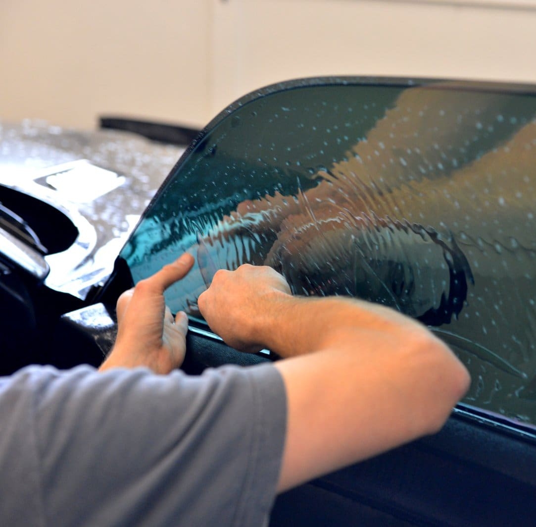 Man uses squeegee to work out bubbles in freshly applied tint on door window