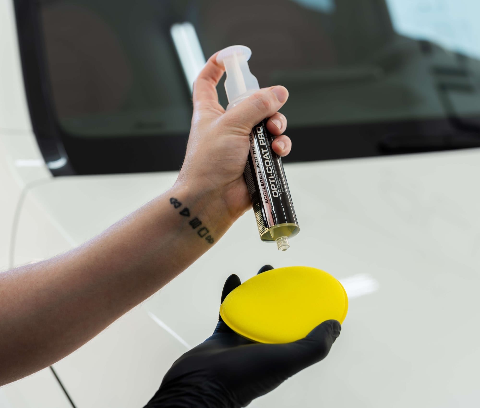 Hand with tattoo on wrist uses syringe to apply OptiCoat ceramic coating to sponge